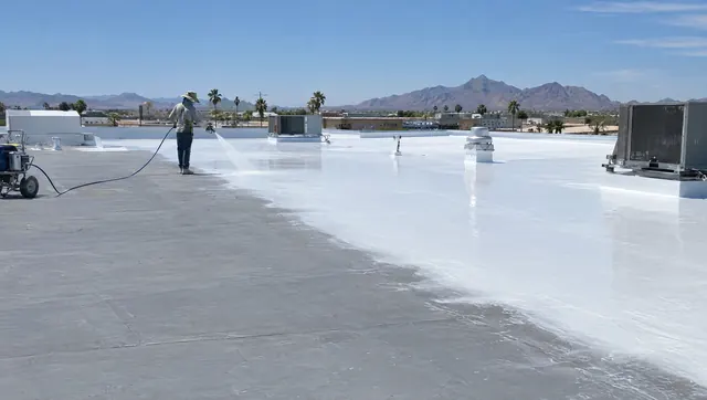 White silicone roof coating being sprayed across a large flat roof in Arizona
