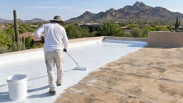 Worker rolling a fresh white recoat over a weathered tan foam roof in Scottsdale